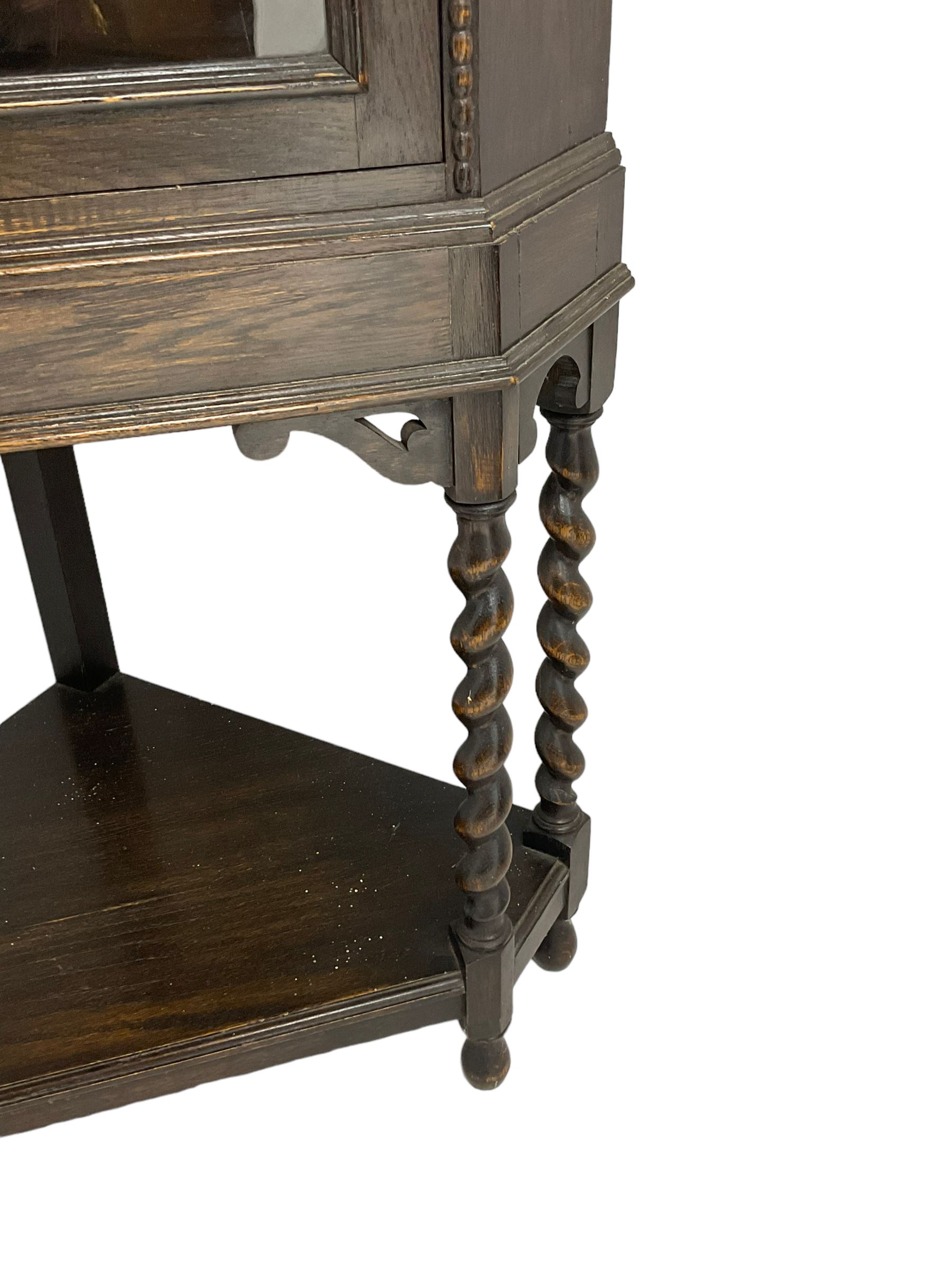 Early 20th century oak corner display cabinet, enclosed by glazed door, on spiral turned supports joined by undertier 
