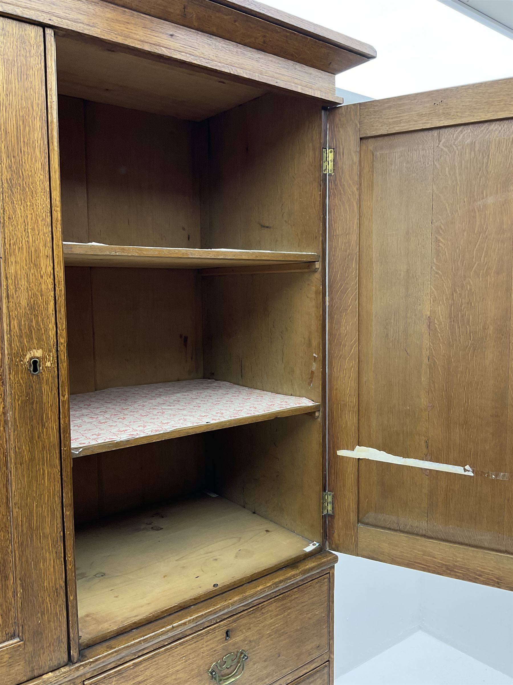 Early 19th century oak linen press cupboard, the projecting cornice over two panelled doors enclosing shelves, two short and two long drawers below, bracket feet
