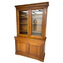 French cherry wood bookcase on cupboard, projecting cornice over two cupboard doors with bevelled glass panels enclosing three adjustable shelves, base fitted with two cushion drawers over double cupboard