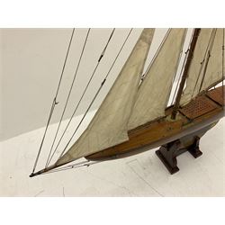 Early 20th century large pond yacht with mahogany hull, stained pine keel with brass rudder, simulated deck hatches and brass fittings, rigged as a staysail schooner (?) with four sails L117cm H148cm; loose mounted on stained pine stand