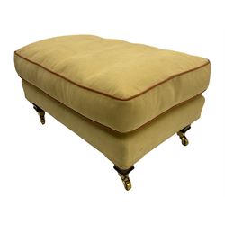 Rectangular footstool, upholstered in pale yellow fabric with peach piping, on mahogany finish feet with brass castors