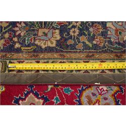 North West Persian Tabriz hand-knotted carpet, madder red field with a central cusped medallion issuing radiating pendants and an all-over design of scrolling arabesques, palmettes and flowering vinery enclosed by conforming spandrels, indigo main border of meandering floral vines and stylized palmettes, flanked by narrow guard stripes, cotton fringe ends 