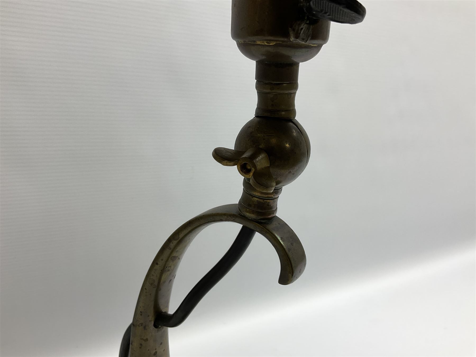 Arts & Crafts Jesson, Birkett & Co, brass table lamp or wall light, designed by Thomas Birkett, the tapering stem with adjustable ball pivot supporting a conical shade with tapering final with ball terminal, upon a circular domed base pierced for wall mounting, shade positioned upright overall H57cm

Often misattributed to Arthur Stansfield Dixon for Birmingham Guild of Handicraft, this particular lamp was designed by Thomas Birkett.
In the late 1890's Birkett worked as a metalwork at the Birmingham Guild, before later joining the Faulkner Bronze Company which went on to become Jesson, Birkett & Co in 1904. The lamp features in lighting catalogues from the firm under the model no E490.

