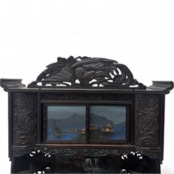 Early 20th century Japanese Meiji style carved hardwood cabinet, of symmetrical tiered form with pierced foliate fretwork panels and phoenix crest, fitted with sliding and hinged doors inset with hand-painted landscape panels depicting Mount Fuji, waterfalls, and lakeside dwellings, raised on shaped bracket supports