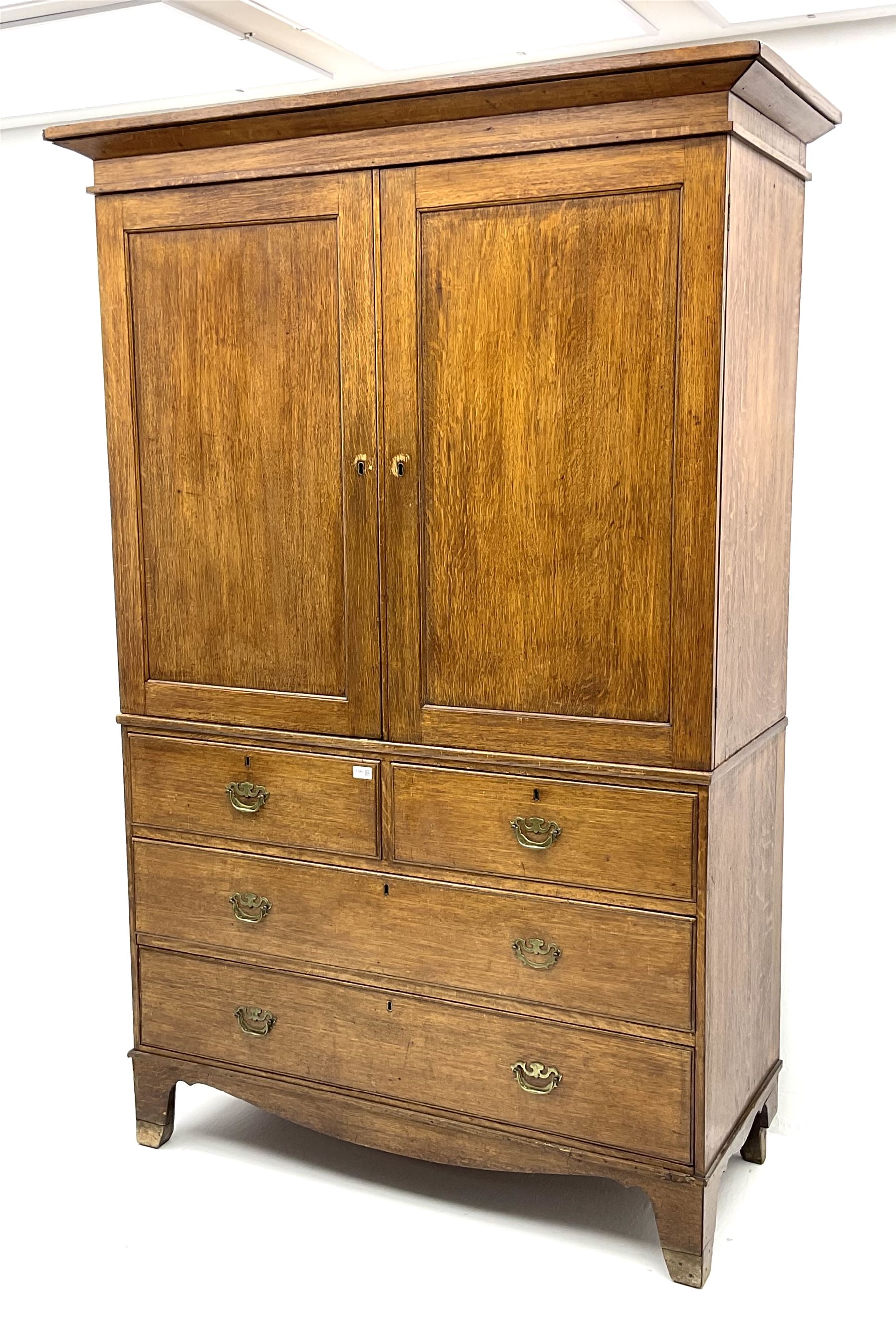 Early 19th century oak linen press cupboard, the projecting cornice over two panelled doors enclosing shelves, two short and two long drawers below, bracket feet
