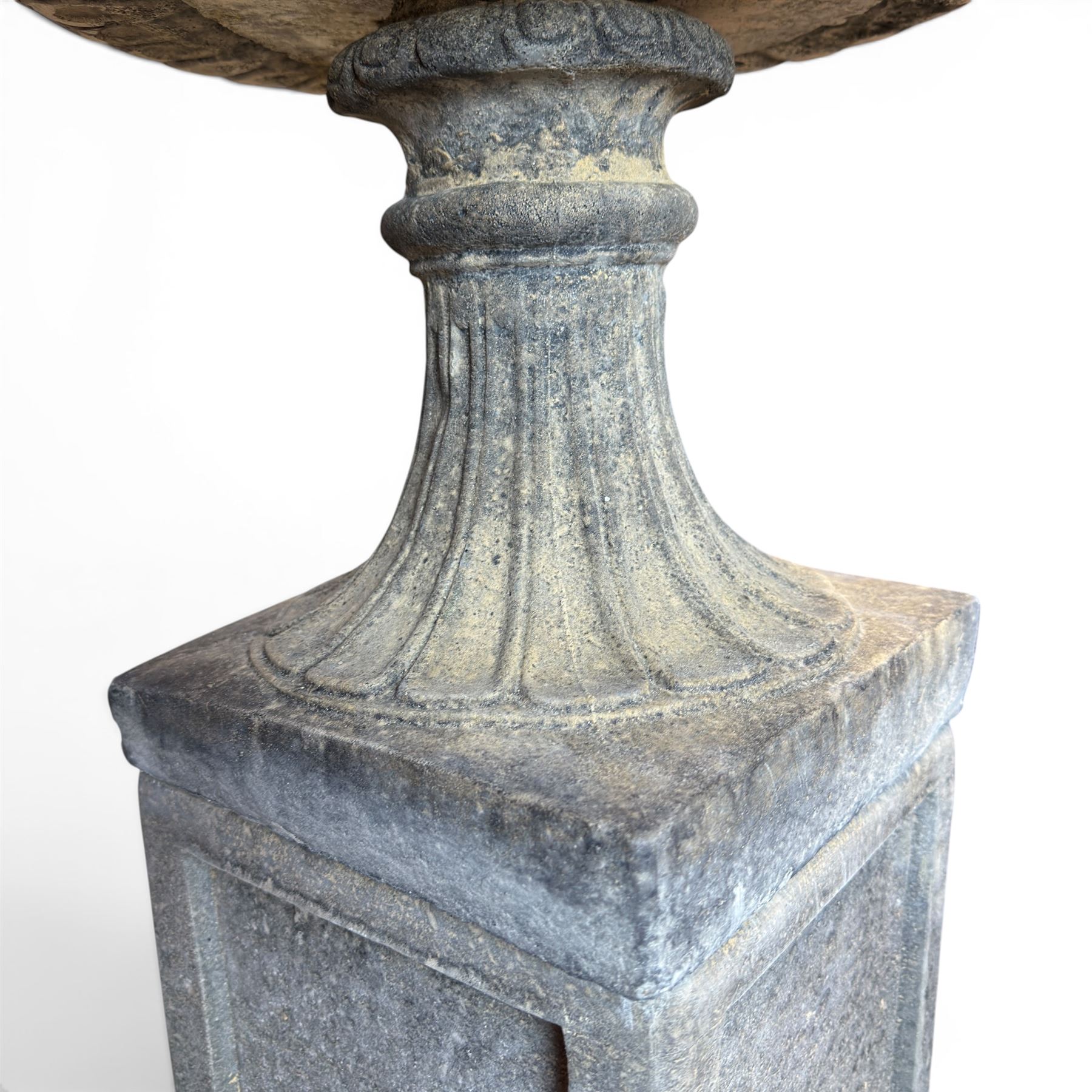 Pair of cast stone garden urns of kylix form on pedestals, the broad egg-and-dart moulded rim over a shallow gadrooned underbelly, with waisted tapering base, raised on matching plinth bases with faux panelled facia