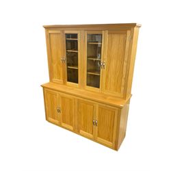 Light oak wall display cabinet, the top section fitted with two double cupboards enclosed by glazed and panelled doors, the lower section with two panelled double cupboards