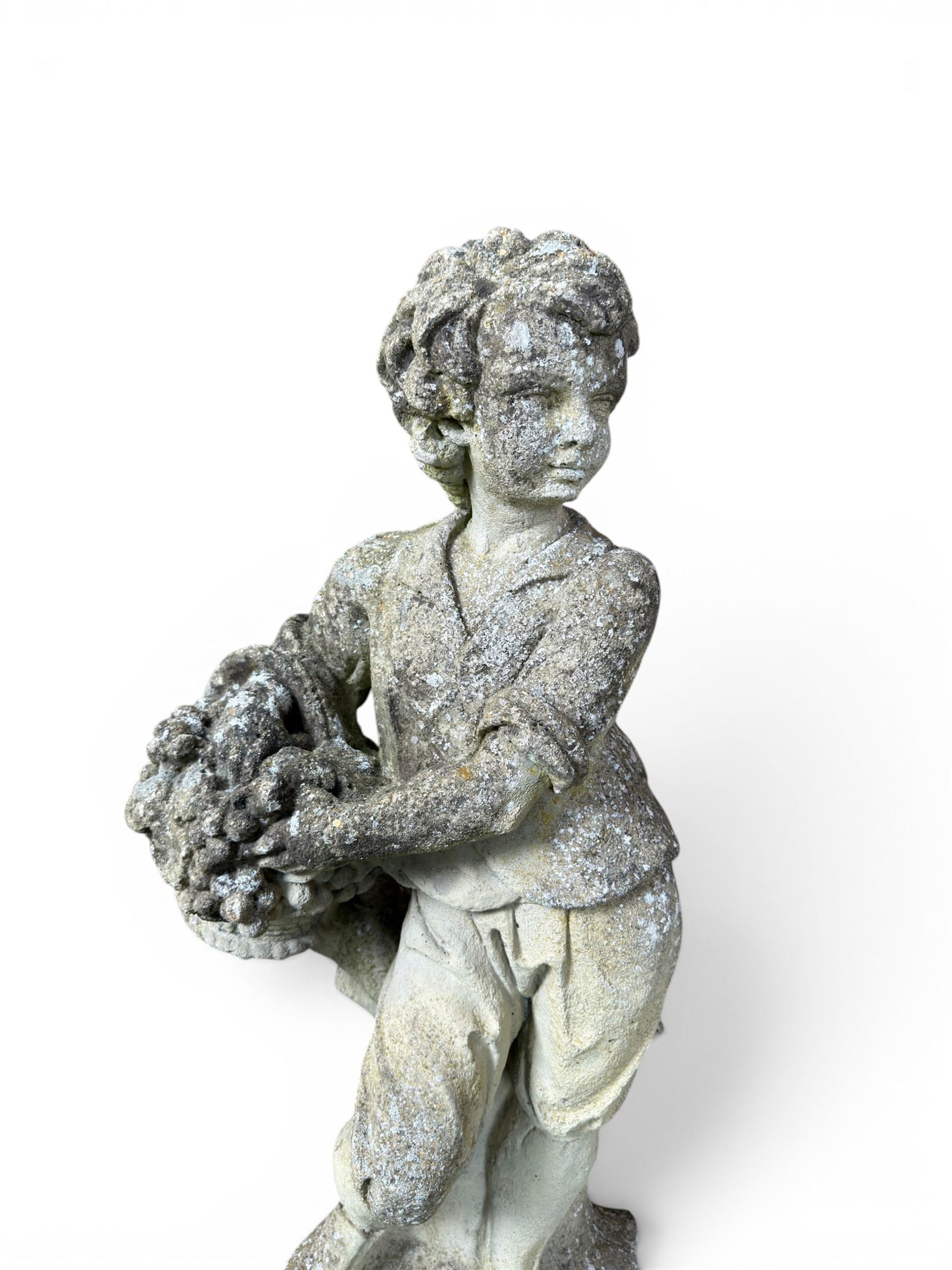 Weathered cast stone garden figure depicting a child holding a fruit basket