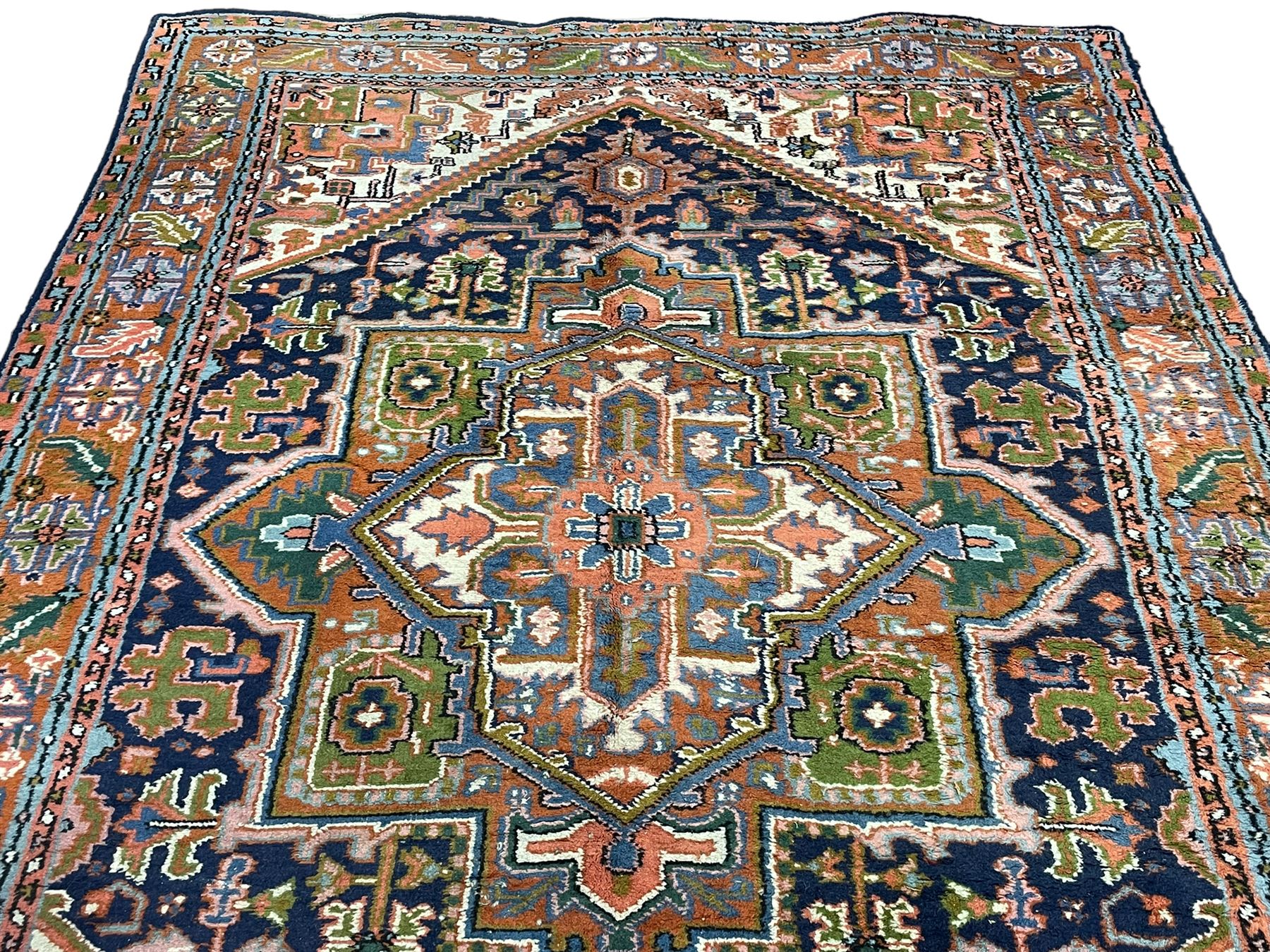 Persian Heriz indigo and rust ground rug, central geometric star medallion decorated with stylised foliate motifs, the border decorated with stylised flower heads