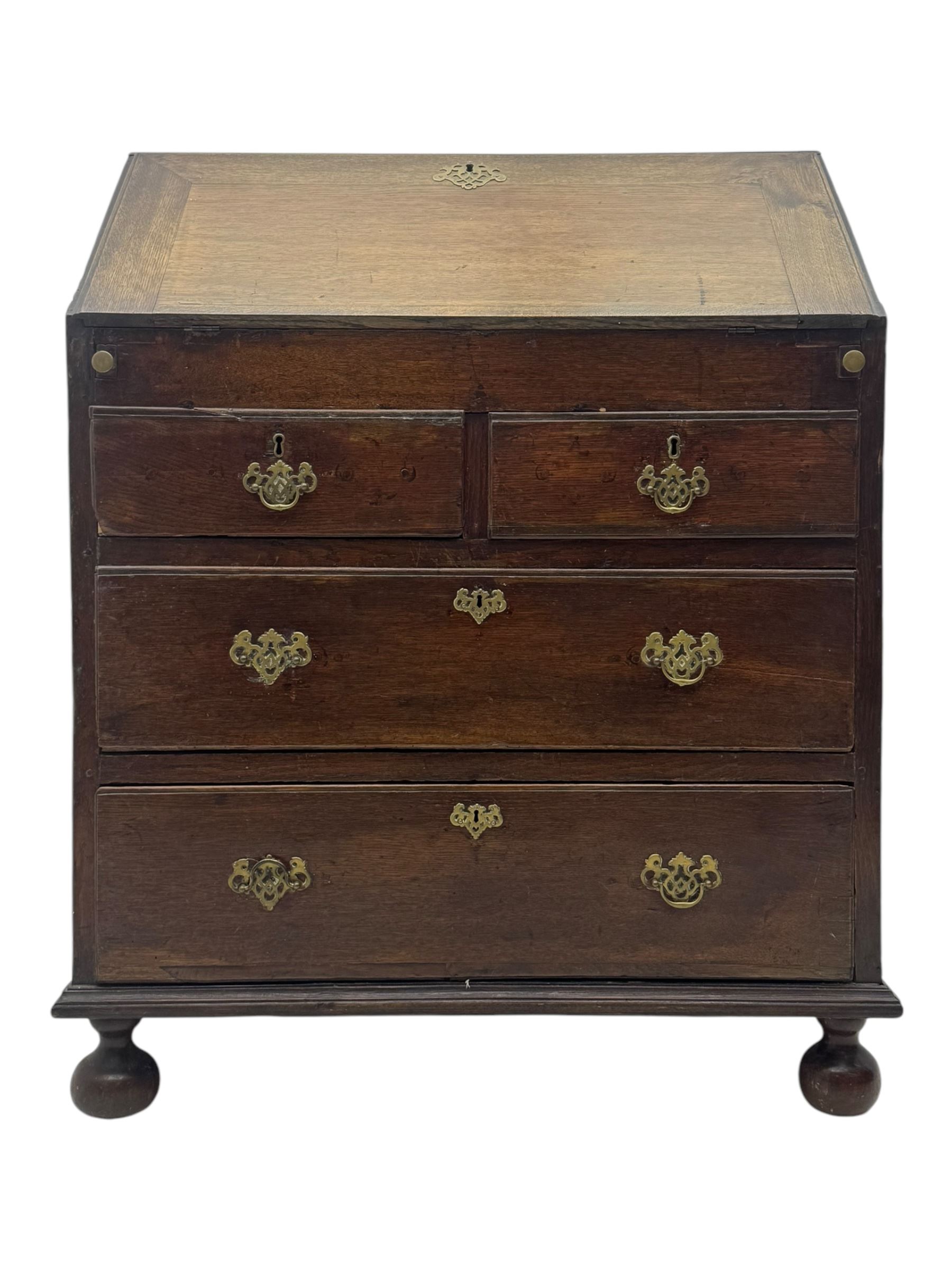 George III oak bureau, sloped fall-front enclosing a fitted interior with pigeonholes, small drawers, and a central compartment, over two short and two long drawers, brass escutcheons and drop handles, raised on bun feet