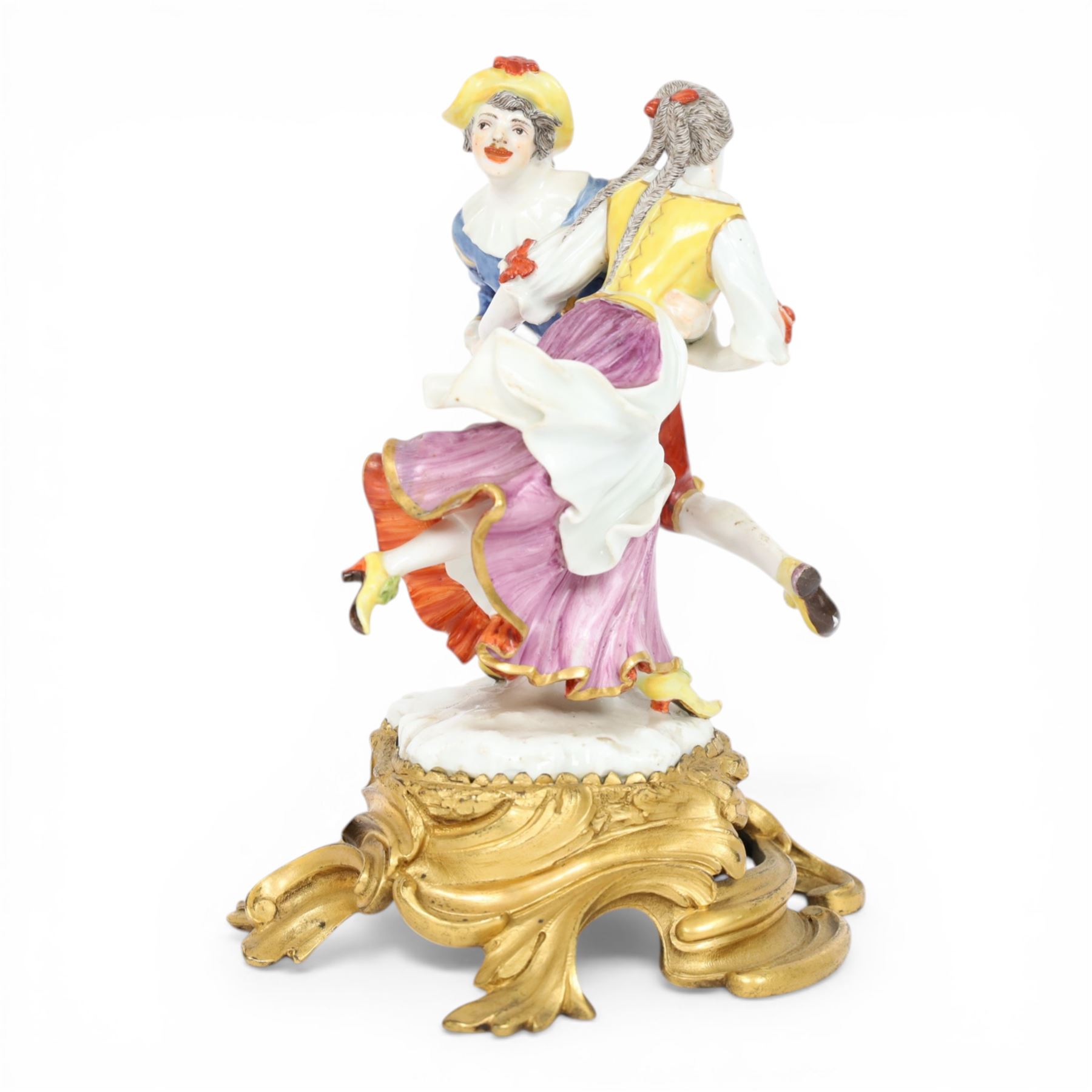Mid 18th century Meissen figure group, The Tyrolean Dancers, circa 1740, modelled as two swirling figures with their arms linked, he in yellow hat with red rosette, blue jacket, red breeches with red rosette, and yellow shoes with green rosette, she in white blouse with red ribbons, yellow and red bodice, white apron over puce skirt and yellow shoes with green rosettes, her hair fashioned into two plaits secured by red ribbon, upon a shaped mound base, within a scrolling gilt metal mount, with blue crossed swords mark to base, overall H19cm
