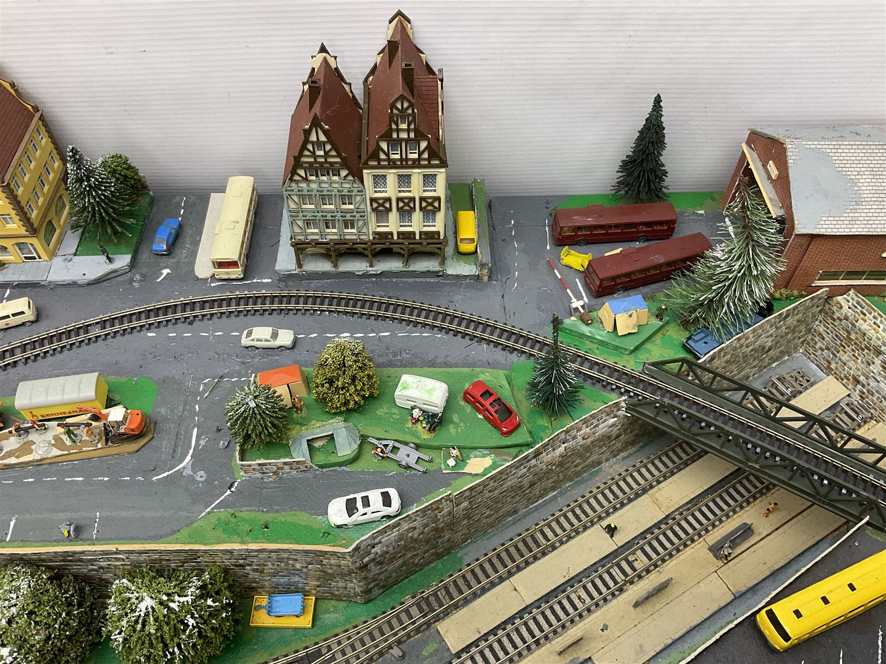 Table top 'N' gauge continental scenic layout as a split level town with various loops of track, station with numerous platforms, engine shed, assorted buildings, roads with motor vehicles and figures, tunnels, trees, river with bridge, tram depot etc 122 x 52cm