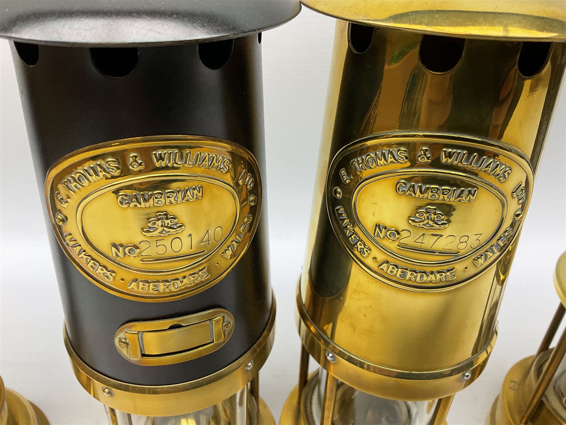 Four miners lamps, comprising Clanny miners lamp, with flip top and gauze protected by three rods, stamped E.T.W E-3, lamp with a gauze chamber protected by three rods, and two E. Thomas & Williams Ltd lamps, tallest example H26cm