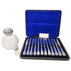 Set of twelve early 20th century silver handled butter knives, hallmarked William Yates Ltd, Sheffield 1919, contained within a fitted leather case with blue silk and velvet lined interior, together with two clear cut glass bottles with silver covers, comprising facet cut scent bottle with foliate embossed cover and glass stopper, hallmarked London 1923, makers mark worn and indistinct, H6cm, and a dressing table bottle of spherical form with octagonal and hobnail cut decoration, the cover embossed with flower heads and C scrolls, hallmarks worn, probably Claydon, Robin & Co, London 1903, H14.5cm