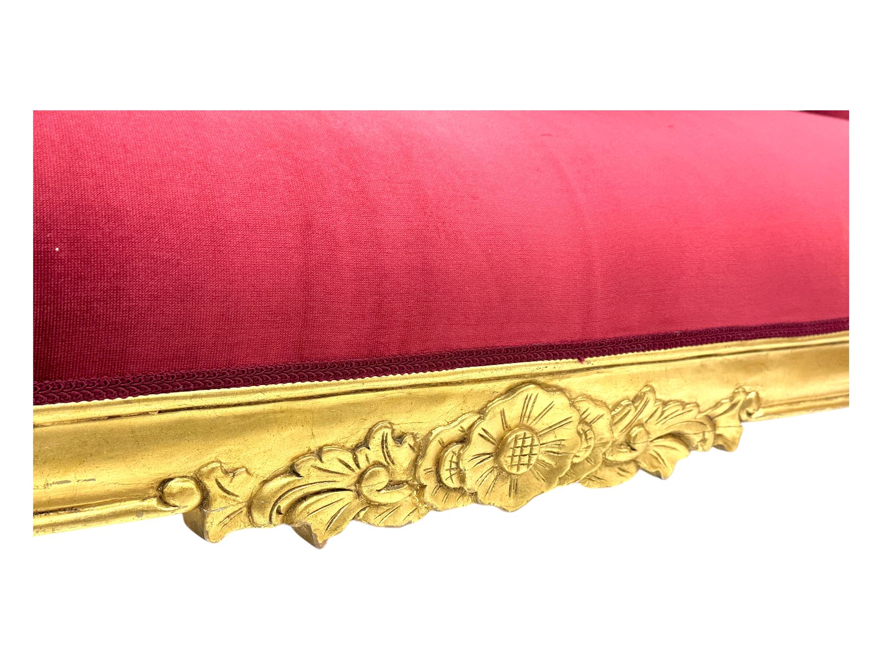 Victorian design giltwood chaise longue, the curved backrest and seat upholstered in deep red velvet with tufted detailing, the frame carved with floral motifs and scrolling acanthus leaves, raised on shaped cabriole supports