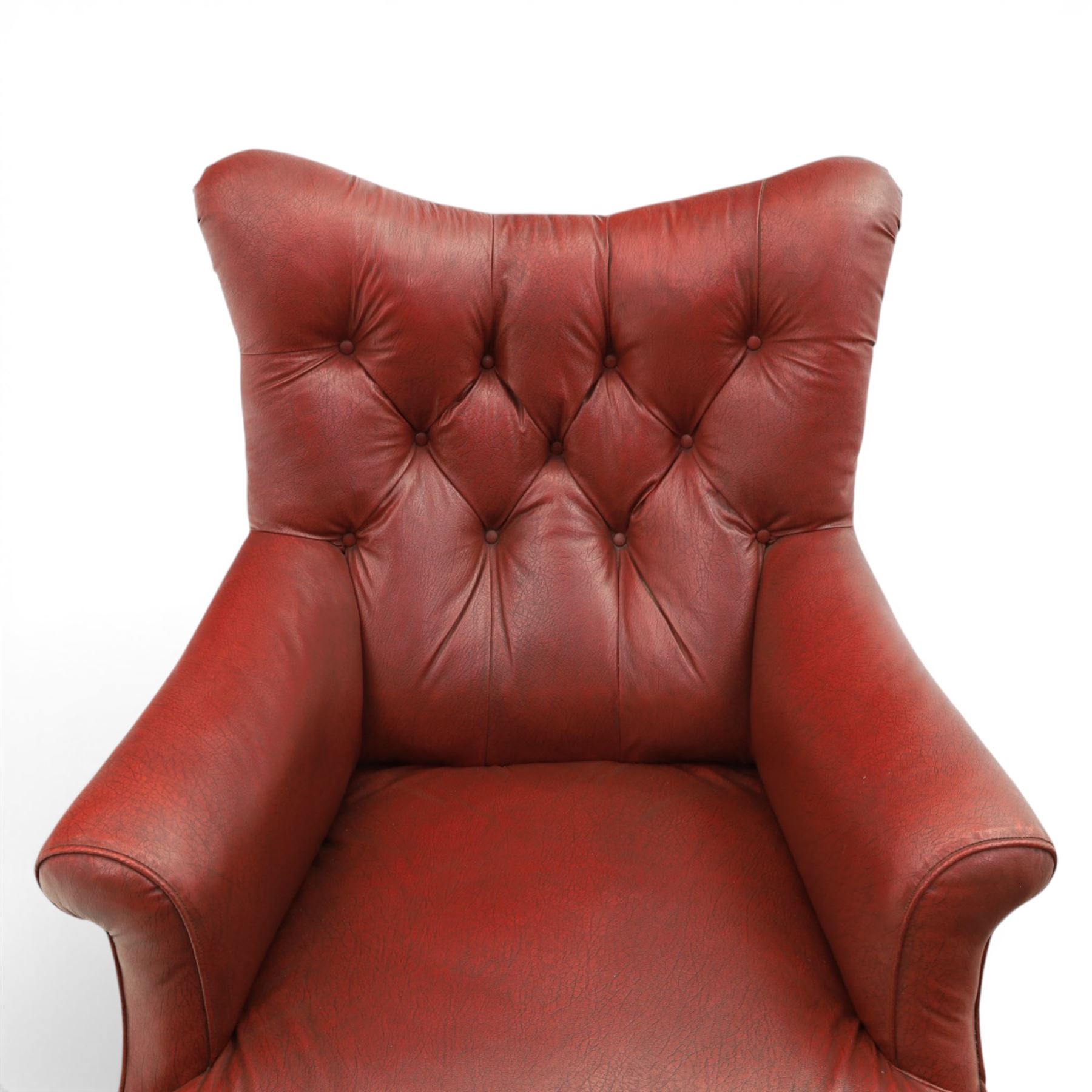 Early 20th century style oxblood red leather Chesterfield armchair, deep buttoned shaped back over padded scroll arms and loose seat cushion, raised on turned mahogany front supports with brass caps and castors