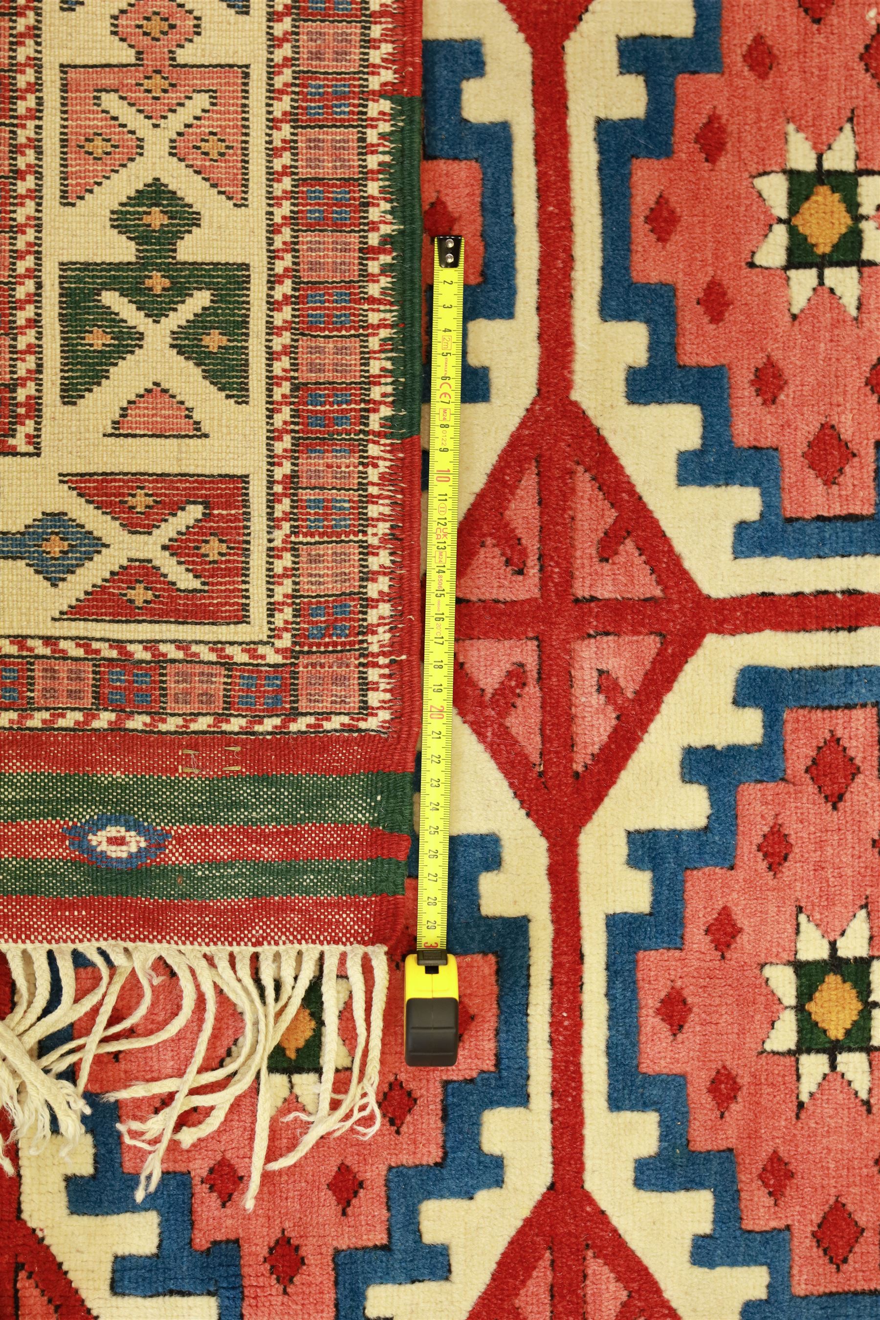 Anatolian Soumak rug, ivory ground decorated with a grid of eight octagonal medallions in terracotta red outlined in blue, centered with a star motif in vertical rows, framed by a series of geometric borders in ivory, green, and blue, incorporating hooked devices and stylized lozenges and stripped end panels, with signature at either end 