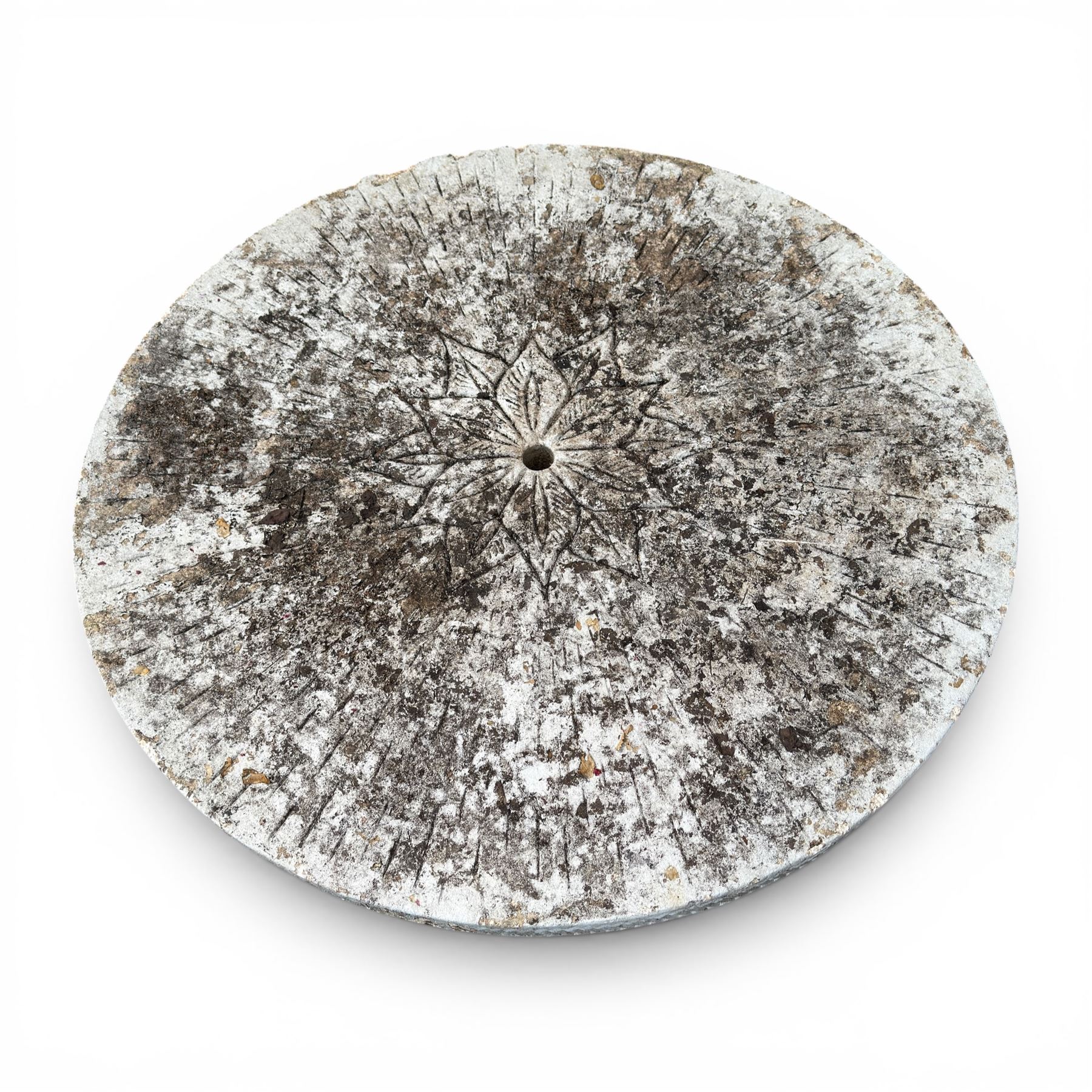 Weathered cast stone garden table, circular top etched with central floral medallion, the edge with repeating chevron motifs, raised on a quadriform S-scroll pedestal with stepped and chevron carved base
