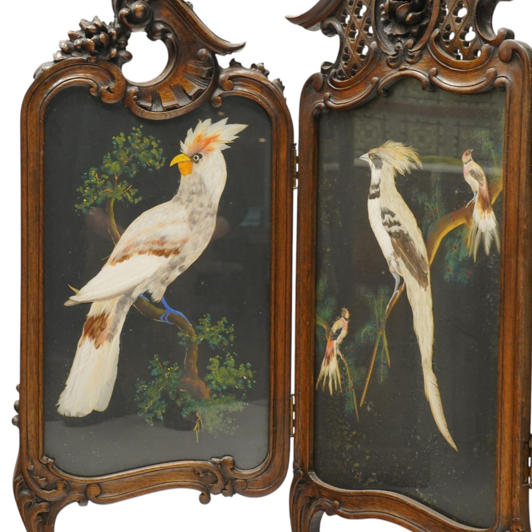 Rococo Revival carved hardwood framed triple panel fire screen, pierced and carved foliate and cartouche pediments with C-scrolls and scallop decoration, over three glazed panels depicting exotic birds of Mexican feather art, on cabriole supports with scroll feet