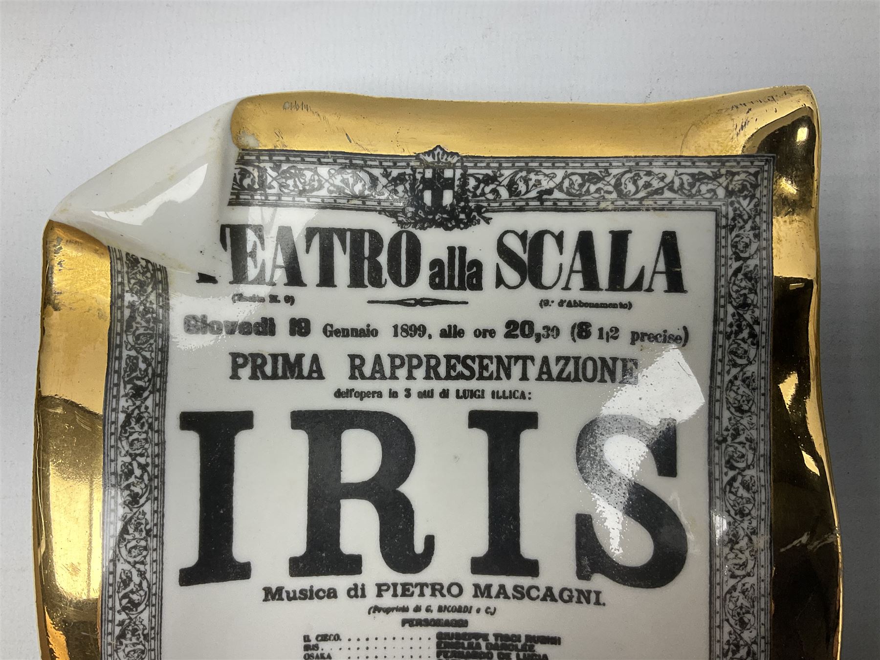 Two Fornasetti rectangular operatic posters ashtrays 'Norma' and 'Iris' decorated with black and white text with a gilt border edge, with printed mark beneath, H16cm