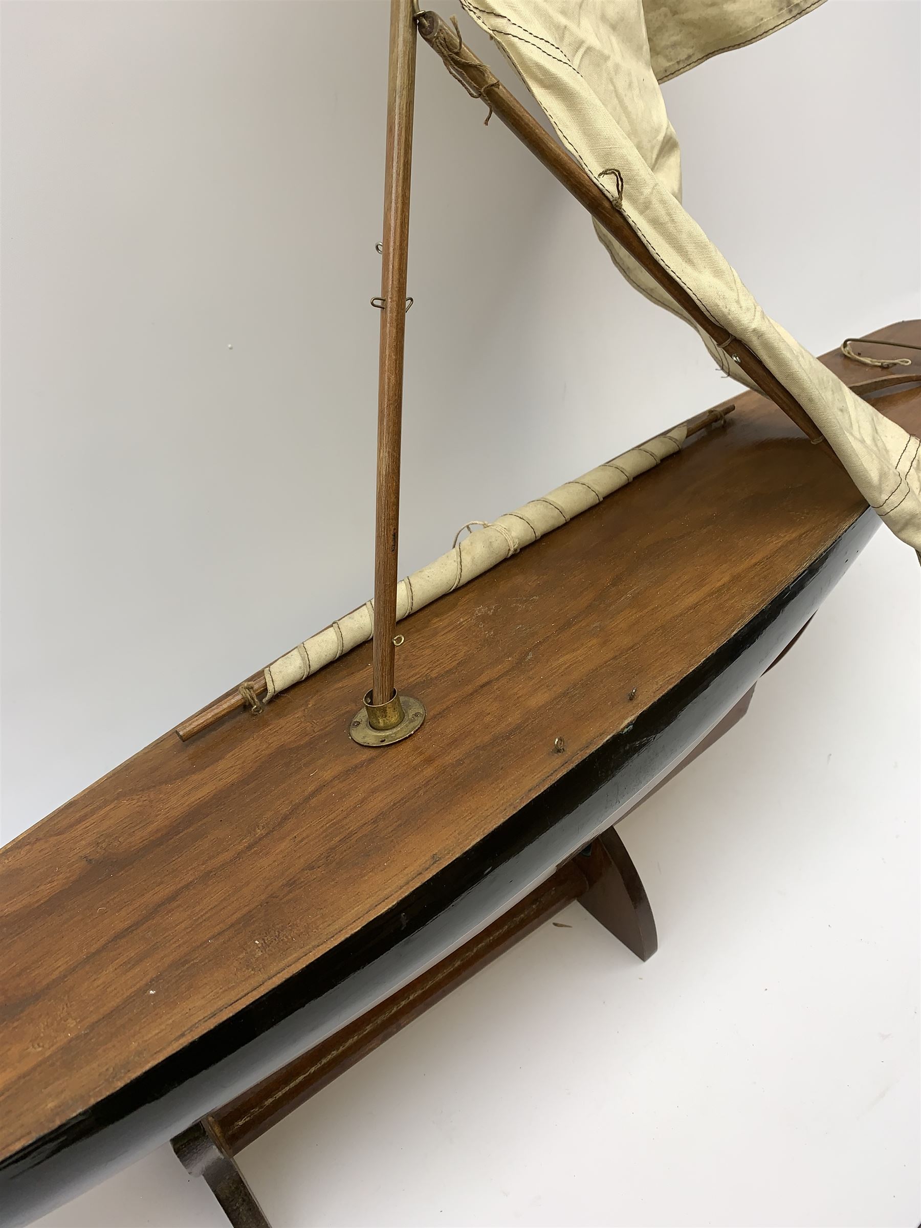 Pond yacht with part black painted mahogany hull and keel, working rudder and mast with three sails W90cm H95cm, loose mounted on mahogany stand