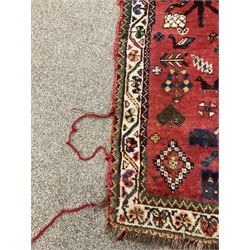 Persian red ground rug, decorated with stylised animal and floral motifs