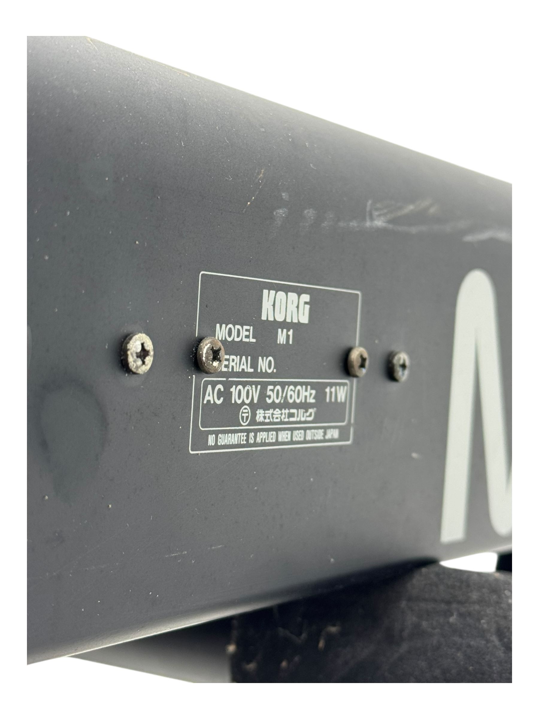 Korg M1 keyboard synthesiser, 61 velocity-sensitive keys with integrated multi-effects and eight-track sequencer, mounted on an adjustable black tubular X-frame stand with rubber end caps