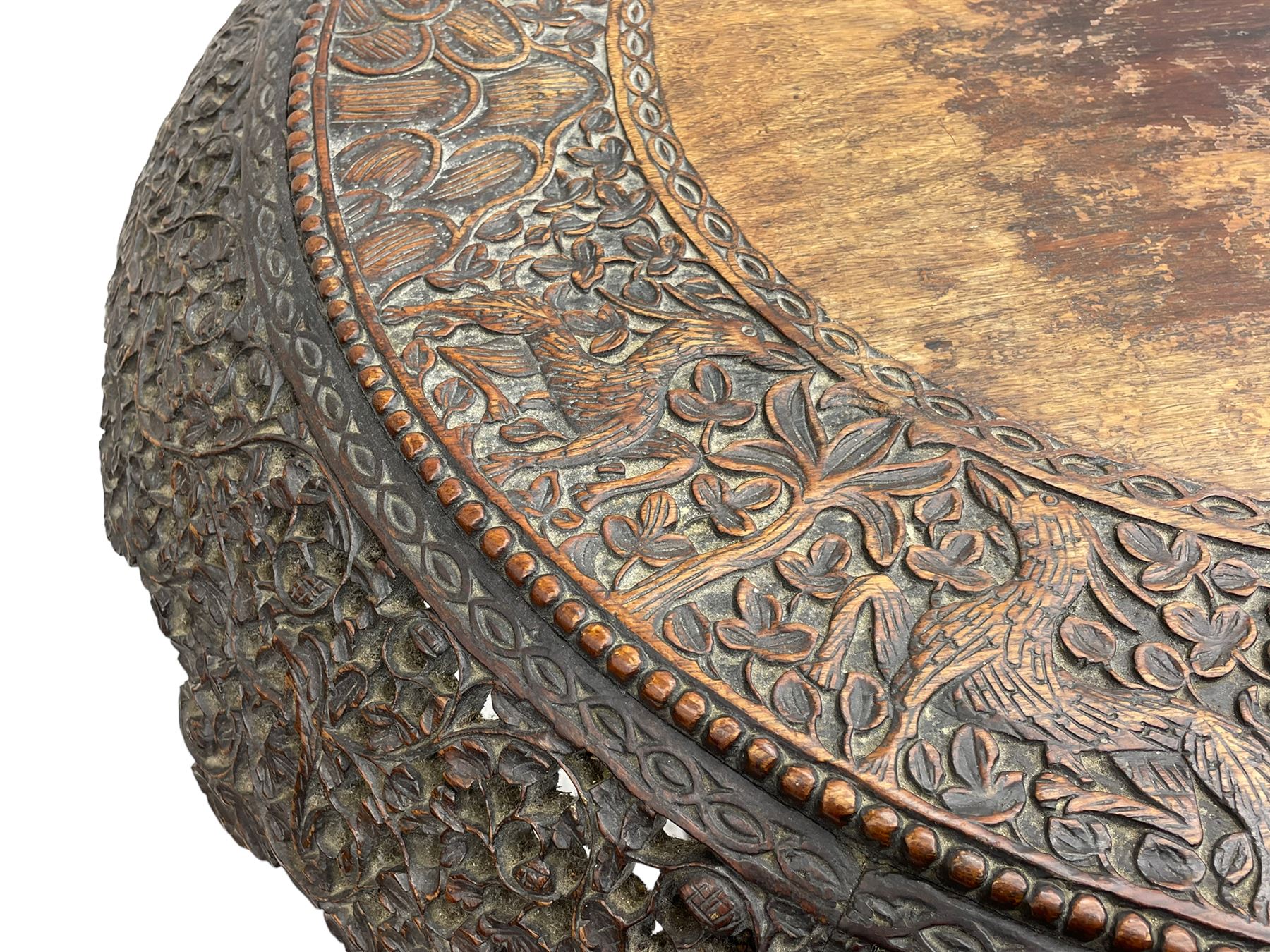 Late 19th century Anglo-Indian carved hardwood occasional table, circular tilt-top carved profusely with mythical animals and foliage decoration, pierced and carved with interlaced leafy branches, leaf carved pedestal supports on a raised platform with further carved and pierced foliage decoration, four carved feet in the form of mythical beasts with gaping jaws 