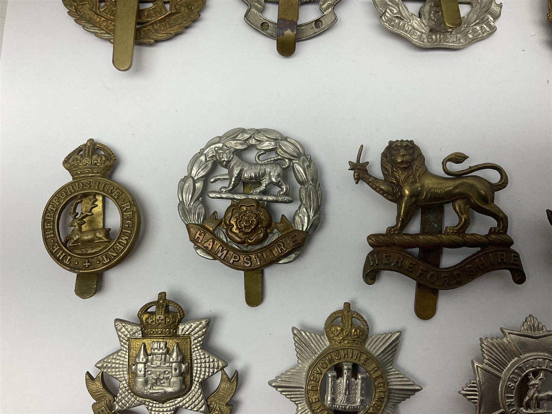 Twenty cap badges including Hertfordshire, Royal Sussex, Cambridgeshire, Hampshire, Notts and Derby, East Surrey, Herefordshire, South Lancashire, Devonshire, Bedfordshire, Durham Light Infantry etc (20)