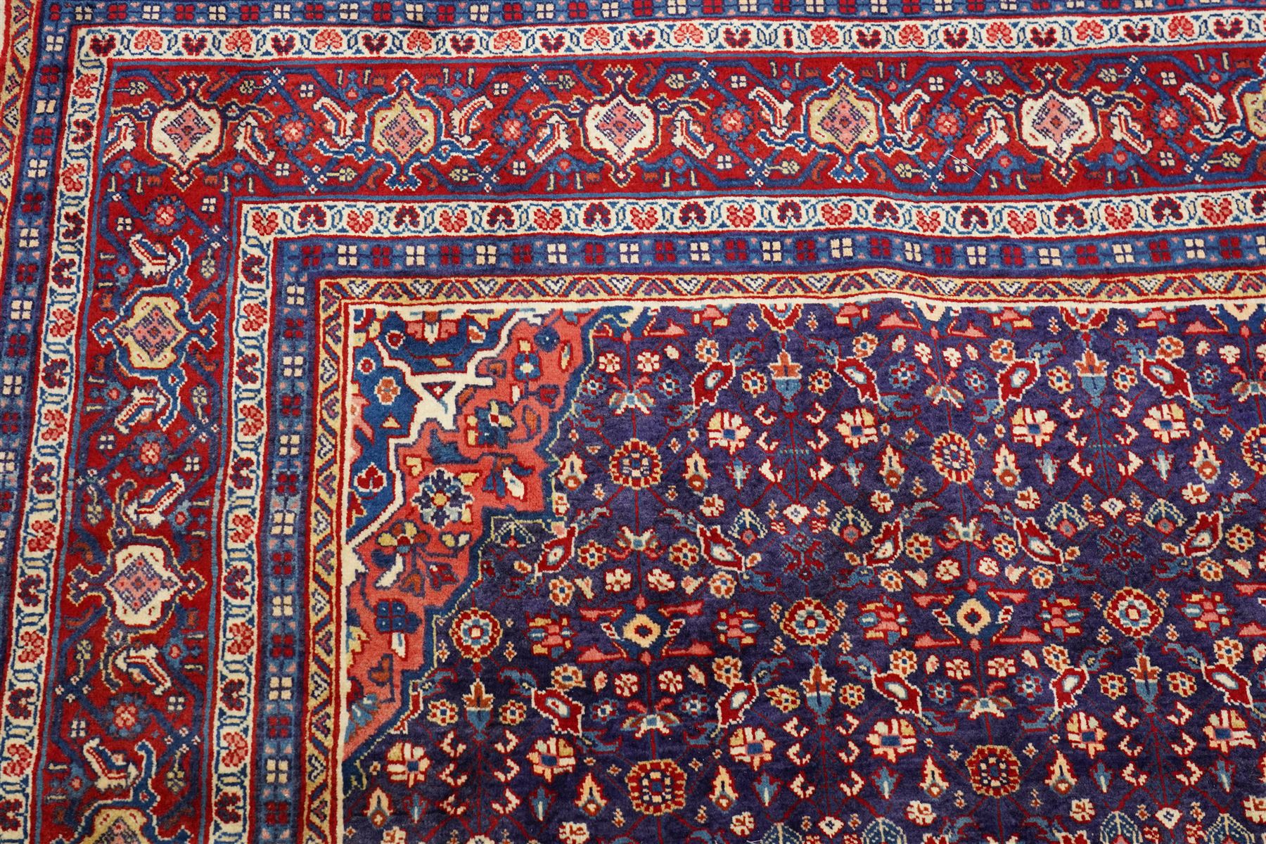 West Persian Mahal hand-knotted carpet, indigo field with central stylized angular medallion issuing an all-over Herati-inspired lattice of floral sprays, rosettes and geometric vinery in tone soft madder red, ivory and soft blue, principal border decorated with stylized palmettes, and angular vine motifs, flanked by multiple guard borders, with cotton fringe ends 