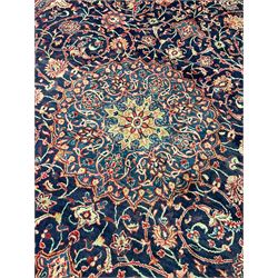 Persian Kashan red and blue ground carpet, the central floral rosette medallion surrounded by interlacing foliate branches and stylised plant motifs, flower head border guards and repeating scrolling main band