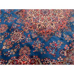 Persian Kirman blue and crimson ground carpet, the field decorated with floral design rosette medallion, the spandrels with scrolling leaf and stylised plant motifs, guarded border decorated with scrolling foliate and flower head motifs, signature panel to one end