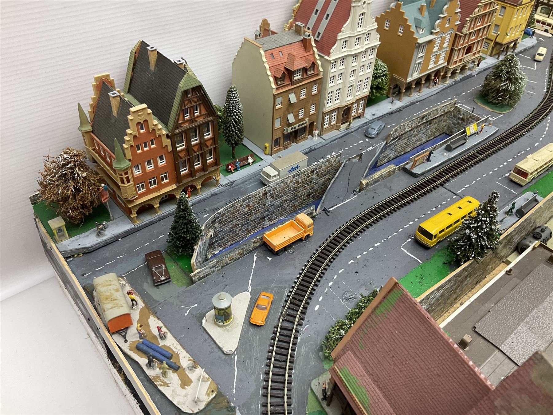 Table top 'N' gauge continental scenic layout as a split level town with various loops of track, station with numerous platforms, engine shed, assorted buildings, roads with motor vehicles and figures, tunnels, trees, river with bridge, tram depot etc 122 x 52cm