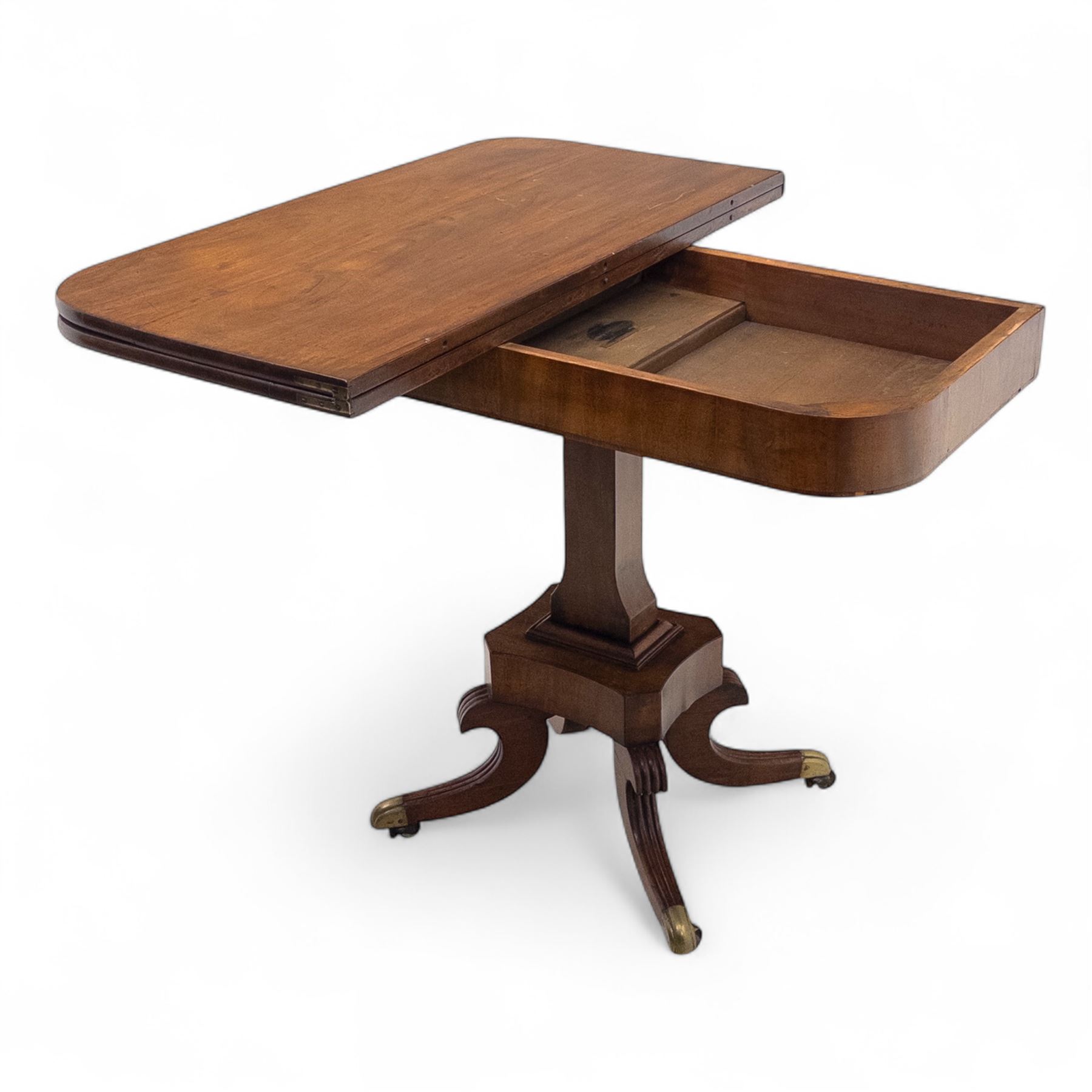 Regency mahogany fold-over table, hinged top with rounded corners opening to reveal a plain polished surface, supported on moulded pedestal base with reeded downswept legs, terminating in brass cups and castors (Extends to 90cm)