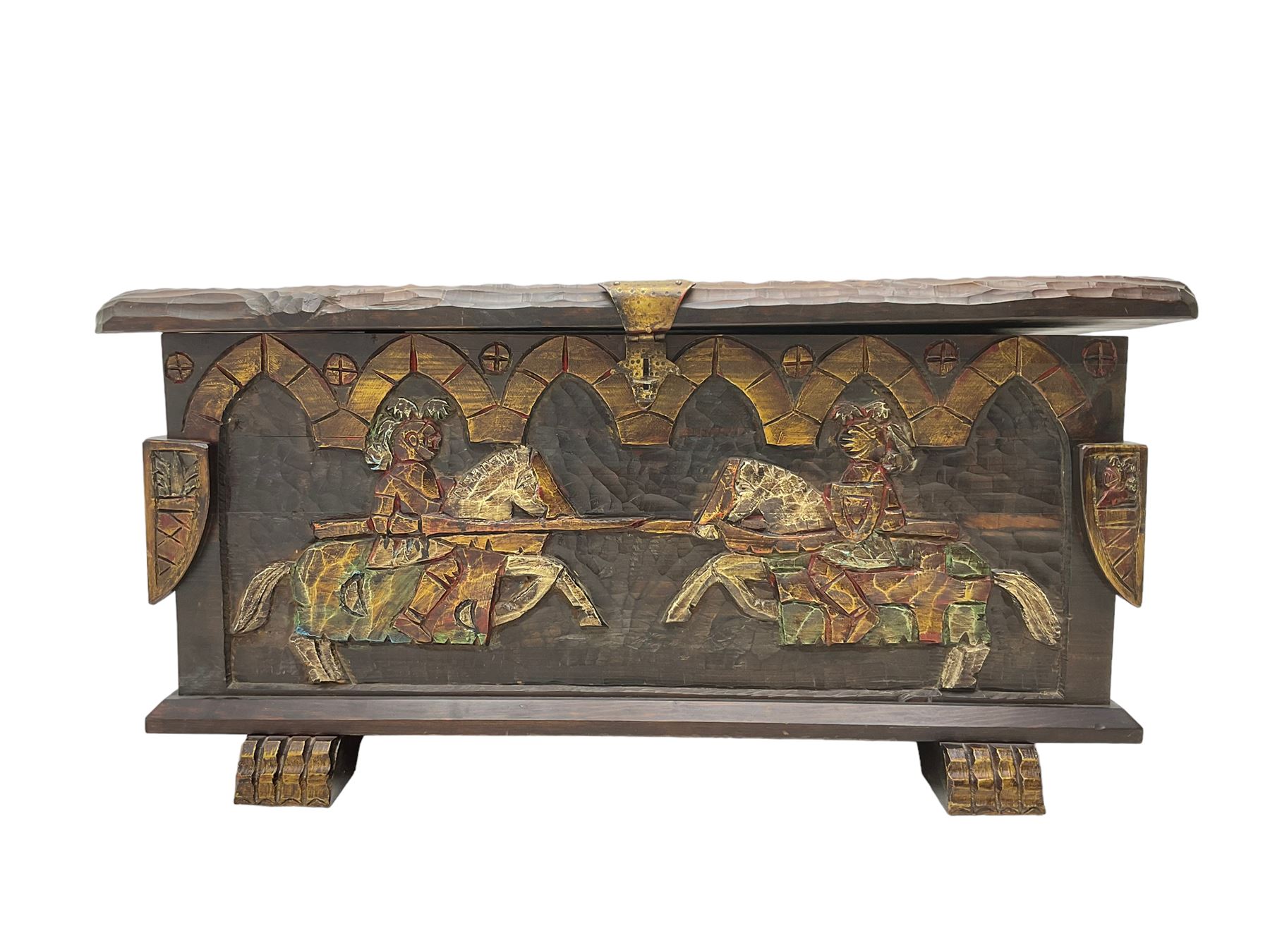 Carved wooden blanket chest, the tooled hinged lid with shaped metal strap hinges and catch, the front carved with arcade over two medieval jousters, on carved sledge feet