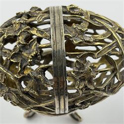 Modern silver limited edition Easter egg, no. 70/500, the gilt openwork body decorated with daffodils and detachable cover with pierced circular panel set with a single faceted blue stone, opening to reveal a gilt interior, upon silver stand with three scrolling pad feet, each hallmarked St James House Company, London 1980, height including stand 8cm