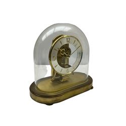 A  late 20th century German Kieninger & Obergfell, “Kundo” battery operated 
mantle clock under an acrylic shade, with an electrically operated solenoid pendulum on an oval brass base with three adjustable feet, visible escapement through an open chapter ring dial, with gilt hands, three-hour numerals and baton markers, with pendulum lock.  H23cm W23cm D13cm
