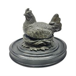 Early 20th century cold painted spelter inkwell, in the form of a hen on nest, upon oval ebonised wooden base, H14cm