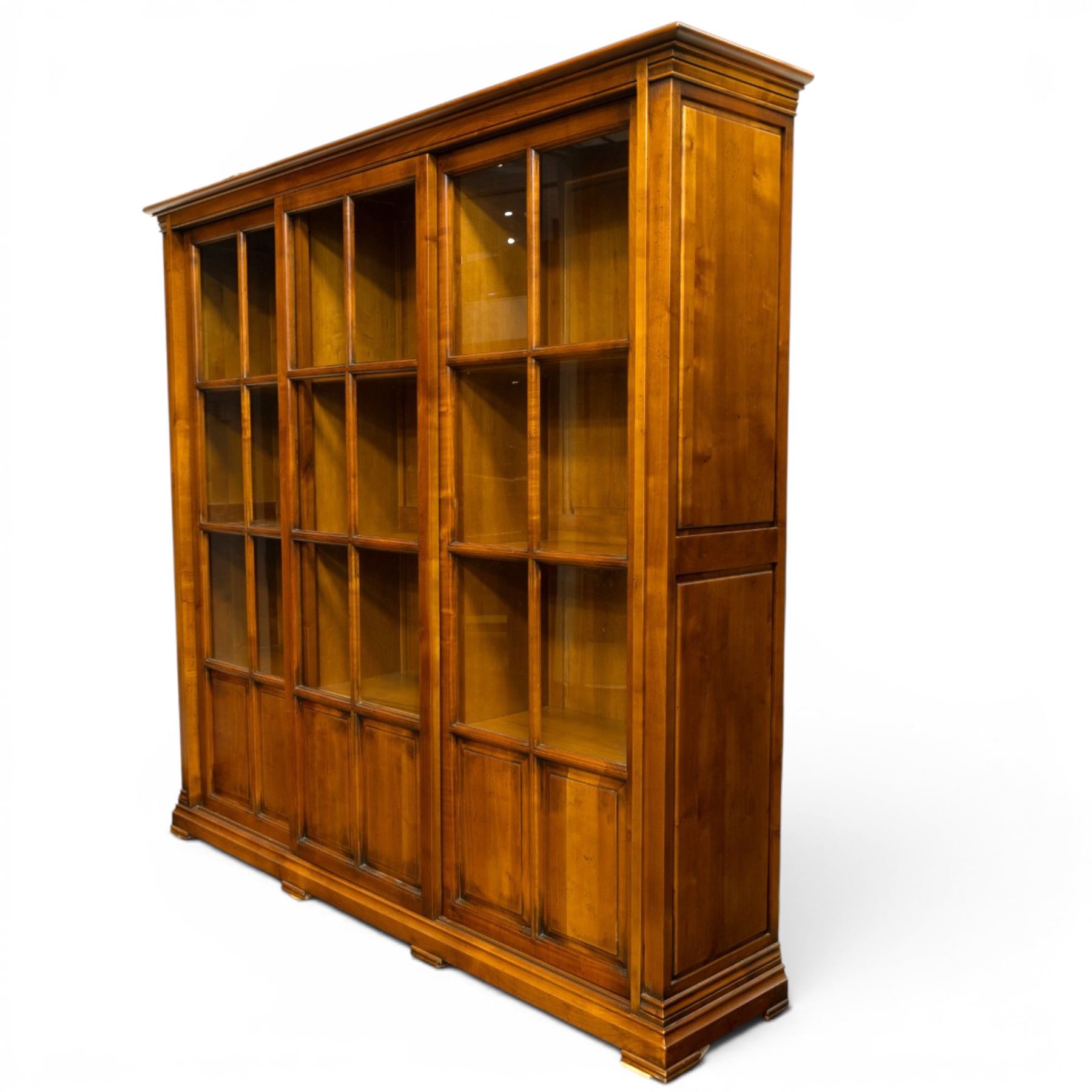 Wesley Barrel - large cherry wood bookcase, with projecting cornice and fielded panelled sides, with three sections comprising three fixed shelves, sliding glazed and panelled doors, moulded plinth base