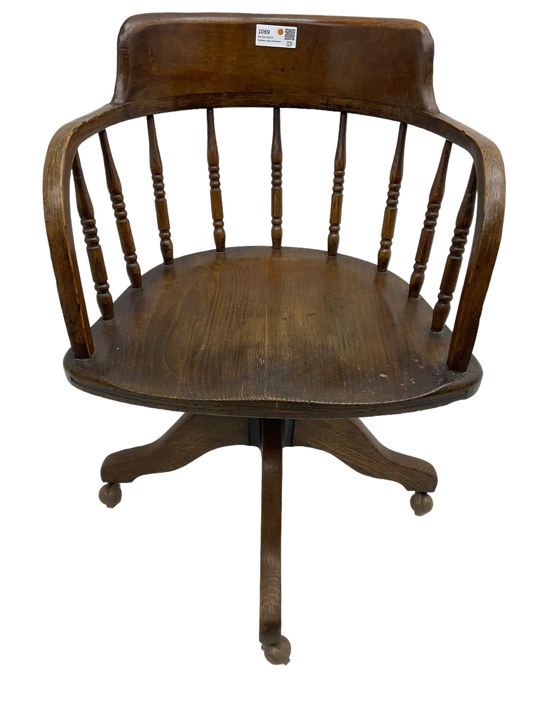 Early 20th century oak framed swivel Captain's chair, tub shaped back with turned spindle supports over saddle shaped seat, quadriform base on castors