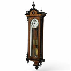 German- Late 19th century twin weight 8-day Vienna wall clock, in a walnut and ebonised case with turned finials and pendants, fully glazed door displaying the the brass cased weights and pendulum, enamel two-part dial with Roman numerals, minute rack, seconds hand and gothic steel hands, rack striking movement with a deadbeat escapement, striking the hours and half-hours on a coiled gong. With key.