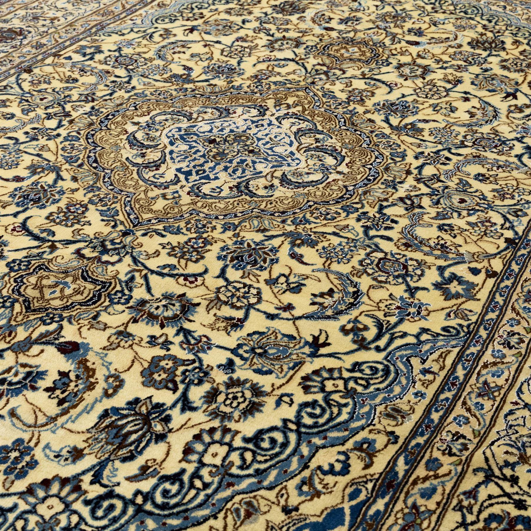 Central Persian Nain hand-knotted carpet, ivory ground, with silk highlights, centred by a shaped floral medallion with pendants, surrounded by scrolling foliate and floral motifs incorporating rosettes, palmettes and delicate vine work in blue, cream and beige tones, enclosed by blue spandrels and an ivory border with repeating palmettes and meandering vines, flanked by floral guard stripes, with cotton fringes