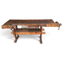 Large early 20th century rustic stained reclaimed pine workbench, the substantial plank top with recessed tool well and two homemade wooden screw vices, above a single frieze drawer and slatted undertier, raised on trestle end supports