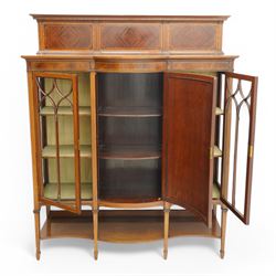 Maple & Co. Edwardian inlaid mahogany display cabinet, raised triple panelled back inlaid with quarter-matched veneers, break bow-fronted top over figured frieze with checkered stringing, enclosed by two astragal glazed doors and central panelled door, oval fan inlay with ribbon tie and trailing bell flowers, on square tapering supports with spade feet united by under tier, with 'Maple & Co.' circular makers plaque to the back