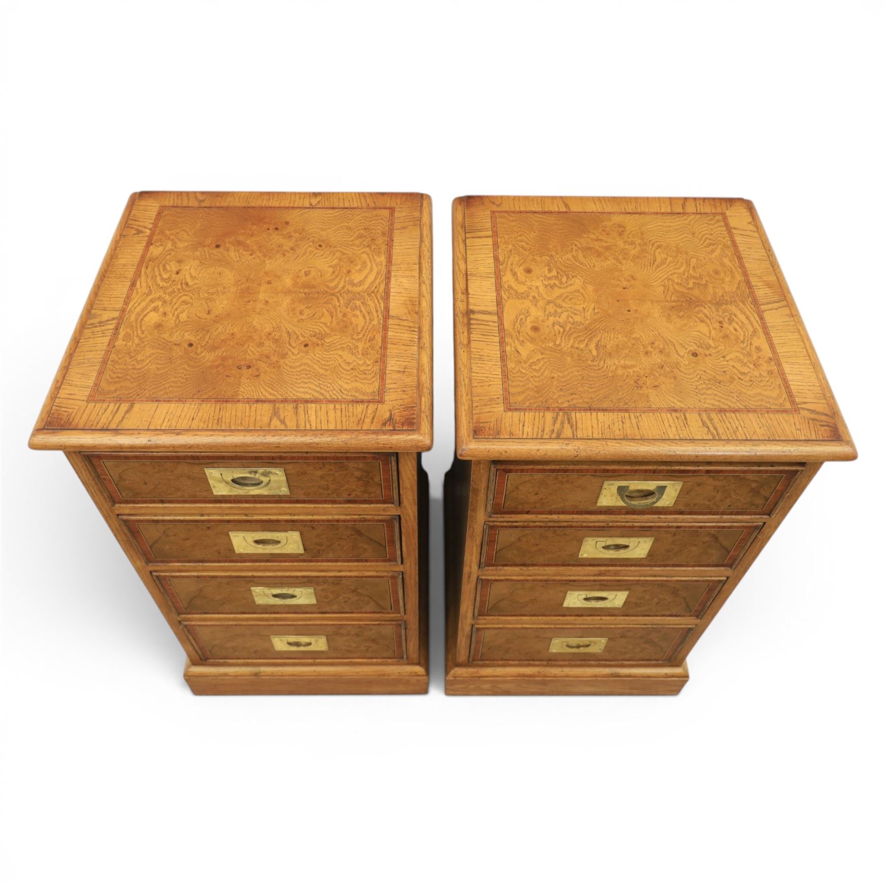 Pair of burr oak bedside tables with campaign brass handles, inlaid and crossbanded top, above four graduating drawers with cockbeaded edges, raised on a plinth base 