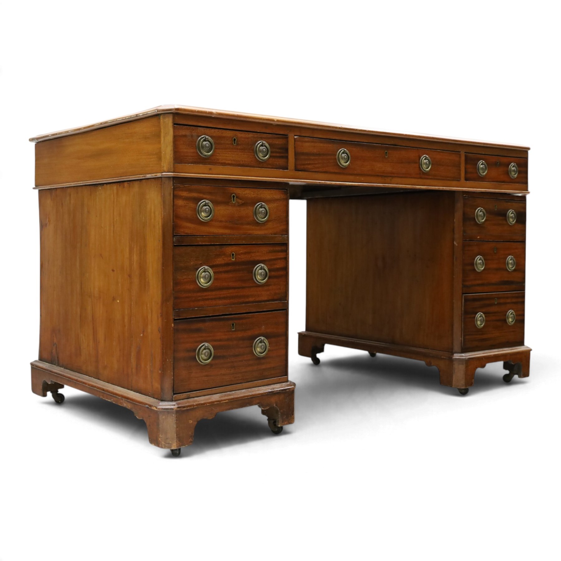 Late Victorian mahogany desk with red leather top, rectangular top with inset toold red leather writing surface, central long frieze drawer flanked by two short drawers, above pedestal with three graduating drawers with ring pull handles, on moulded plinth bases raised on castors