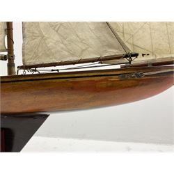Early 20th century large pond yacht with mahogany hull, stained pine keel with brass rudder, simulated deck hatches and brass fittings, rigged as a staysail schooner (?) with four sails L117cm H148cm; loose mounted on stained pine stand