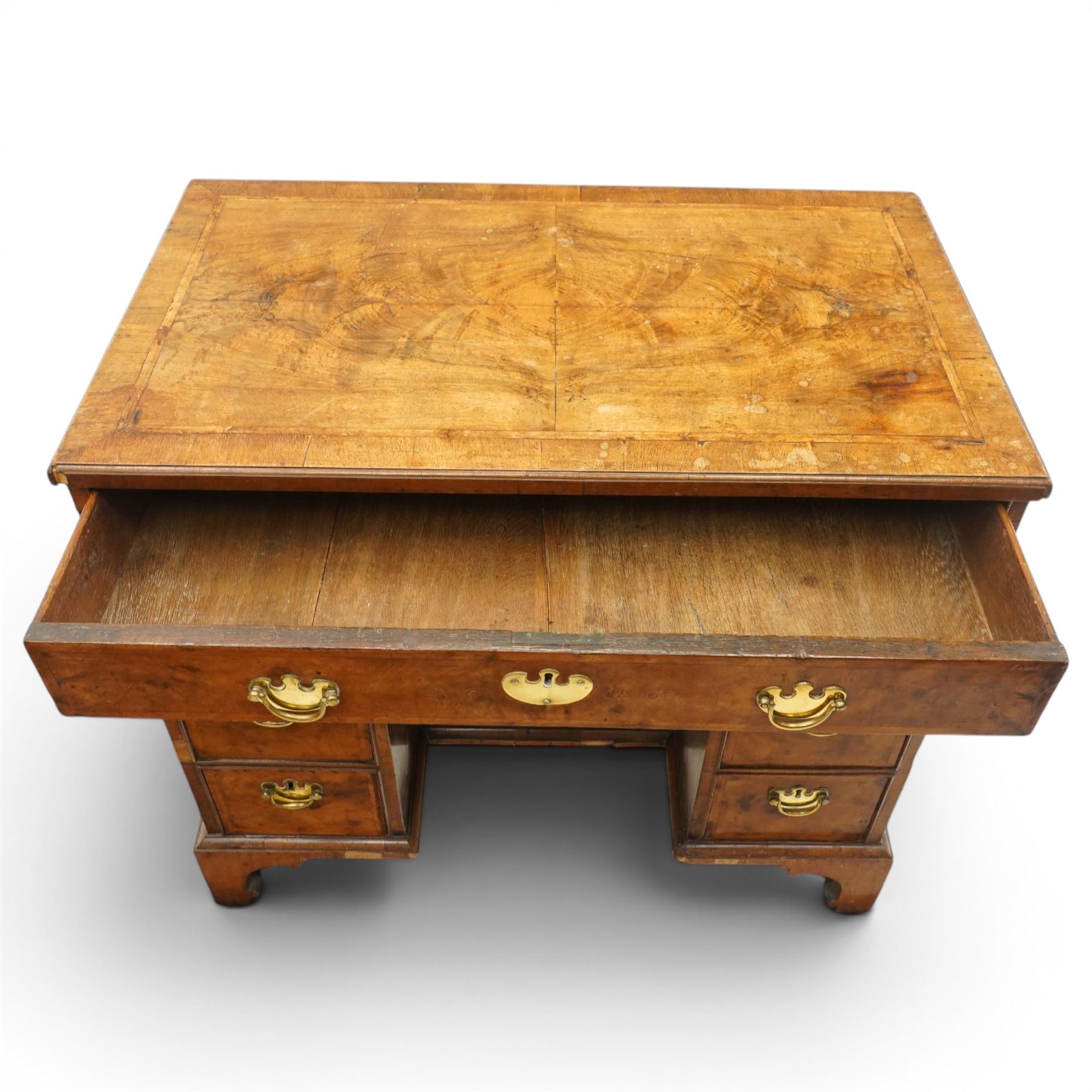 George II figured walnut kneehole desk, the rectangular book-matched veneer top with feather and cross-banding, fitted with single frieze drawer over a short drawer and central recessed cupboard, flanked by three drawers to each side, lower moulded edge on bracket feet