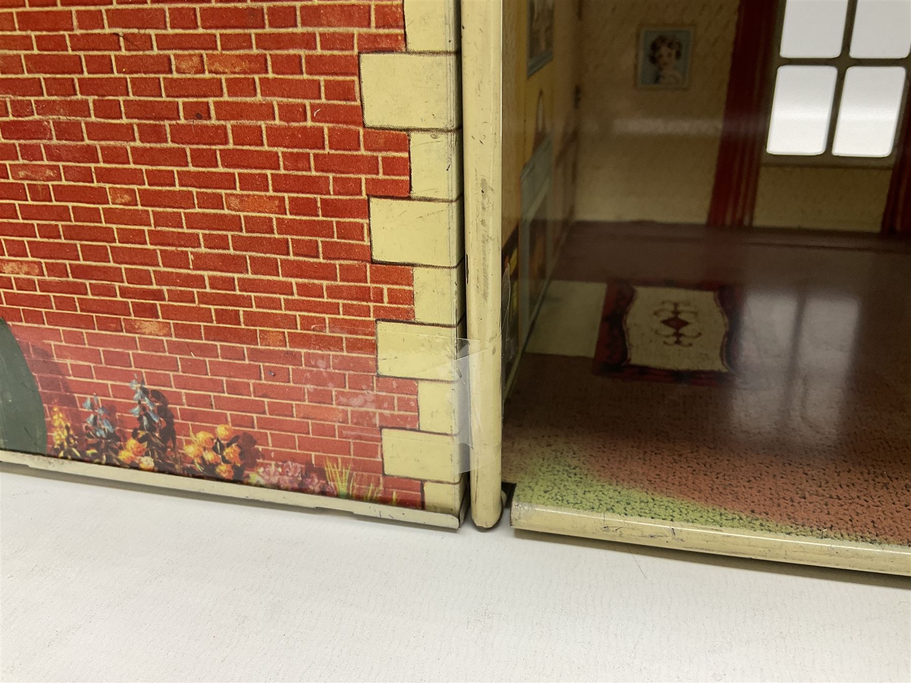 Mid-20th century Mettoy tin-plate double-fronted two-storey doll's house, the front elevation with five unglazed windows flanked by green shutters, central opening door, open back giving access to five rooms together with an attached garage, 60cm wide