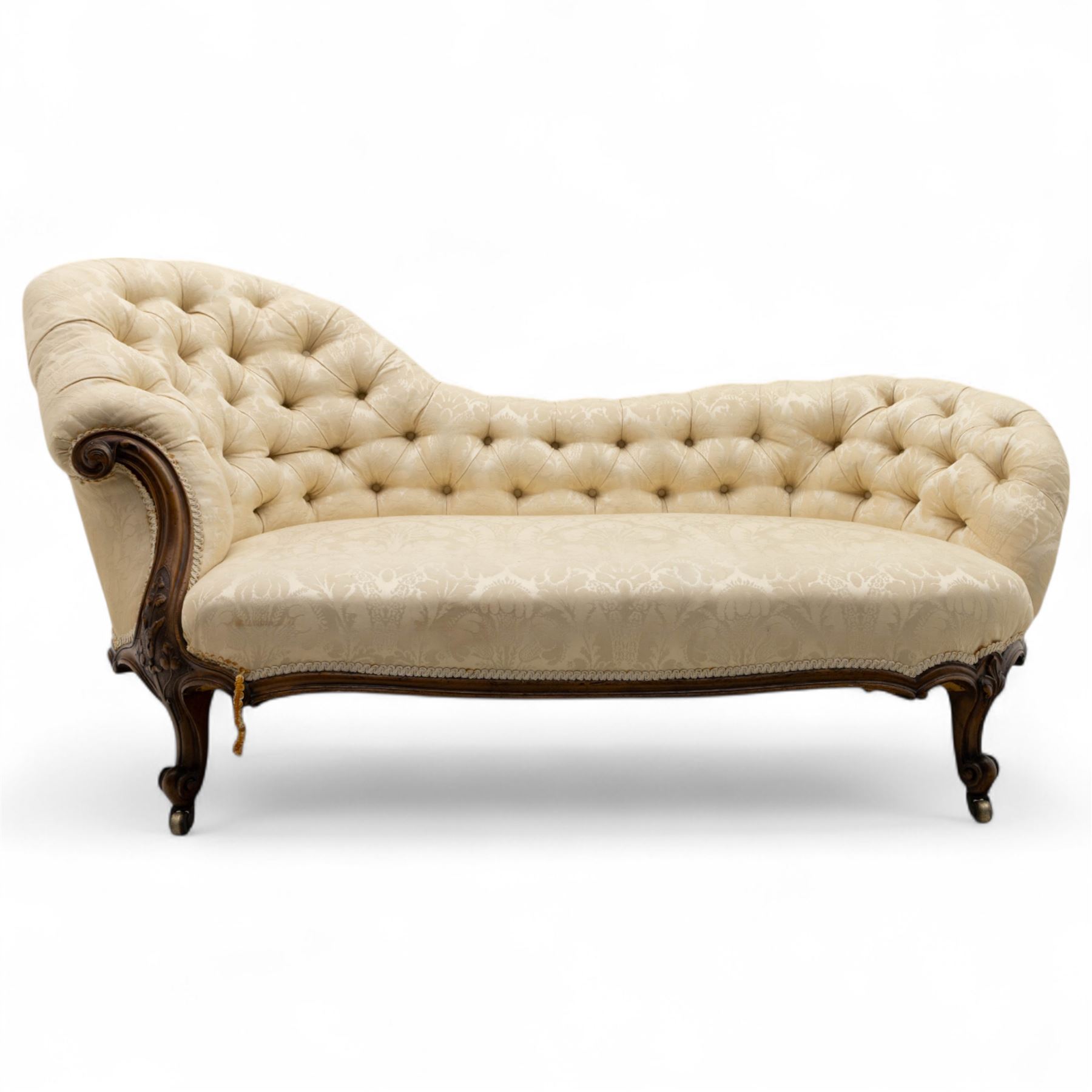 Late 19th century Victorian walnut button-back recamier, asymmetrical form, with cream damask fabric and gimp braid edging, shaped reeded apron above front and back scroll carved cabriole legs on brass castors